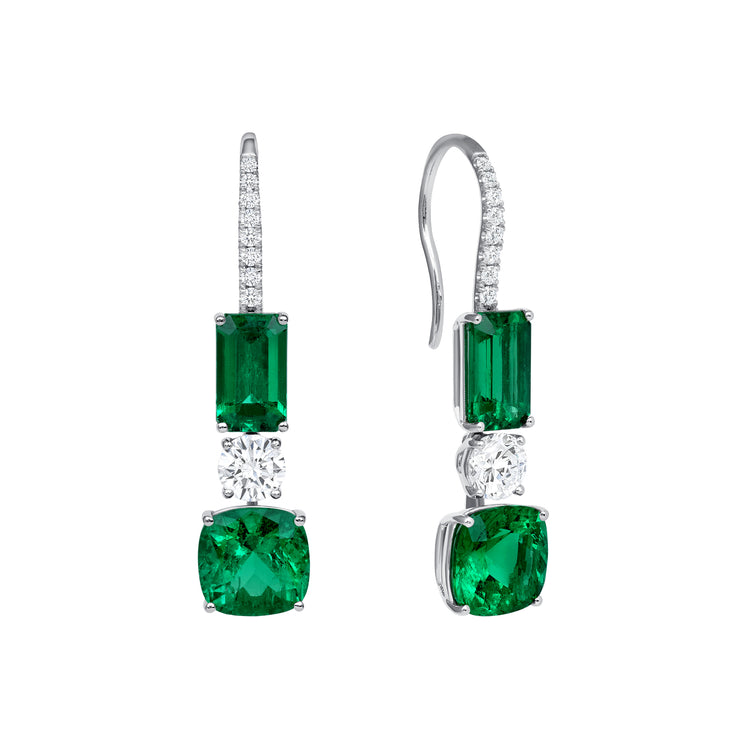 Close up of our Emerald and Diamond Drop Earrings. Featuring cushion cut and emerald cut green emeralds and round diamonds. Set in 18k white gold with a fish hook backing.