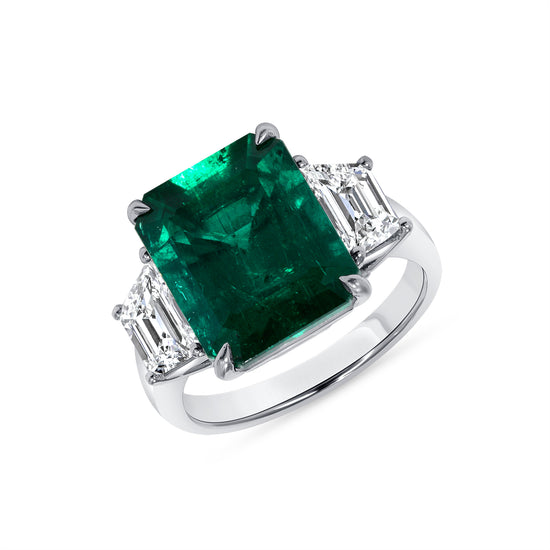 Close up view of the enchanting emerald and diamond engagement ring. Set in platinum, this engagement ring features a central 6.79CT Emerald Cut Emerald and two trapezoid white diamonds.