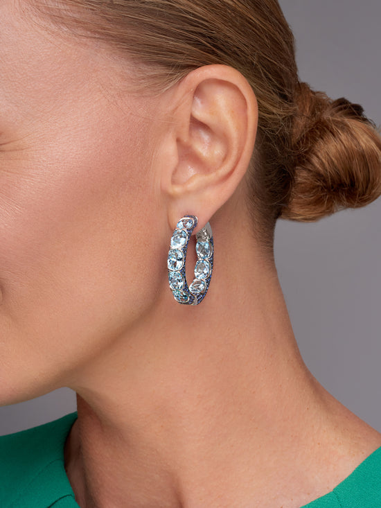 A woman in a tied back bun wearing one Aquamarine Hoop Earring. 