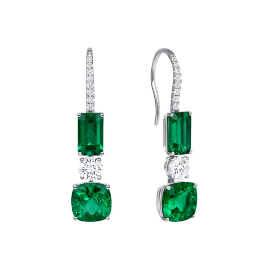 Close up of our Emerald and Diamond Drop Earrings. Featuring cushion cut and emerald cut green emeralds and round diamonds. Set in 18k white gold with a fish hook backing.  