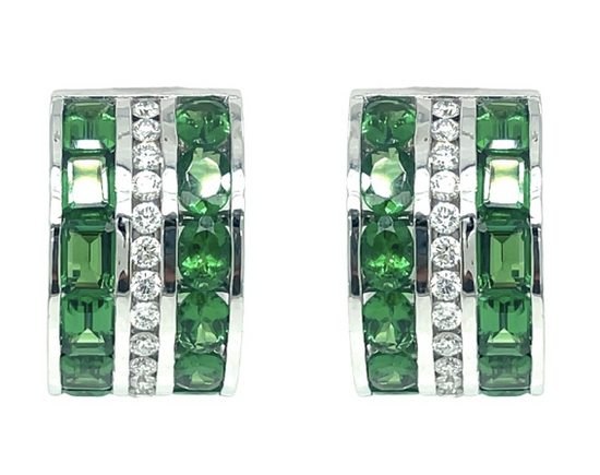 Close up of the Tsavorite and Diamond Huggie Earrinngs. Each earring, set in 18k white gold, features three strips of emerald cut tsavorites, oval cut tsavorites, and round radiant cut diamonds.