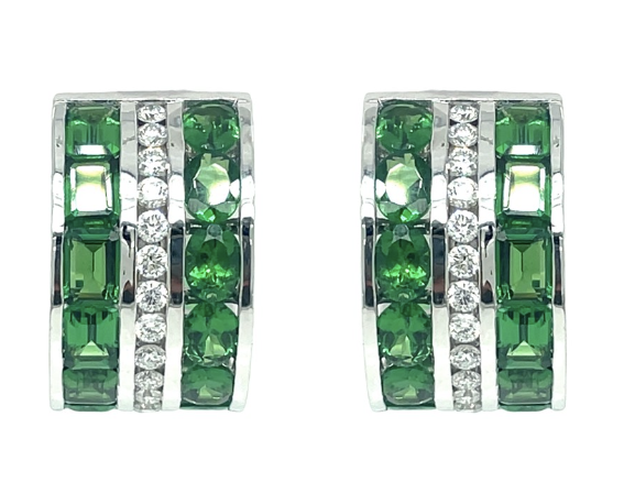 Close up of the Tsavorite and Diamond Huggie Earrinngs. Each earring, set in 18k white gold, features three strips of emerald cut tsavorites, oval cut tsavorites, and round radiant cut diamonds.