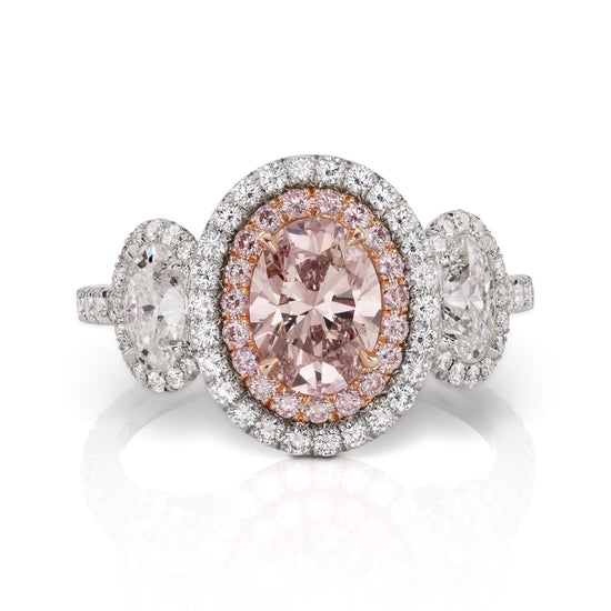 Close up view of the three stone pink oval diamond ring. The center stone is a fancy pink diamond surrounded by a halo of white and pink diamonds. 