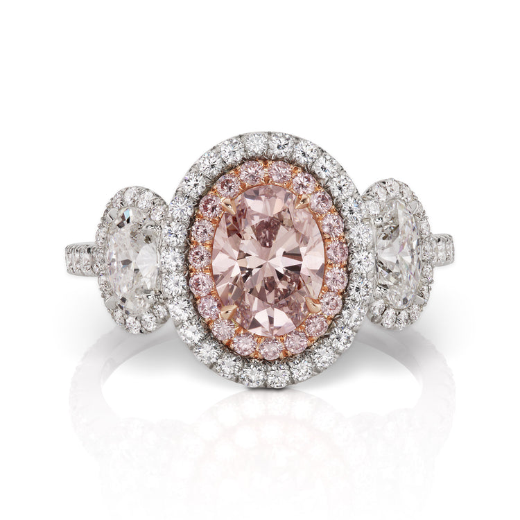 Close up view of the three stone pink oval diamond ring. The center stone is a fancy pink diamond surrounded by a halo of white and pink diamonds. 