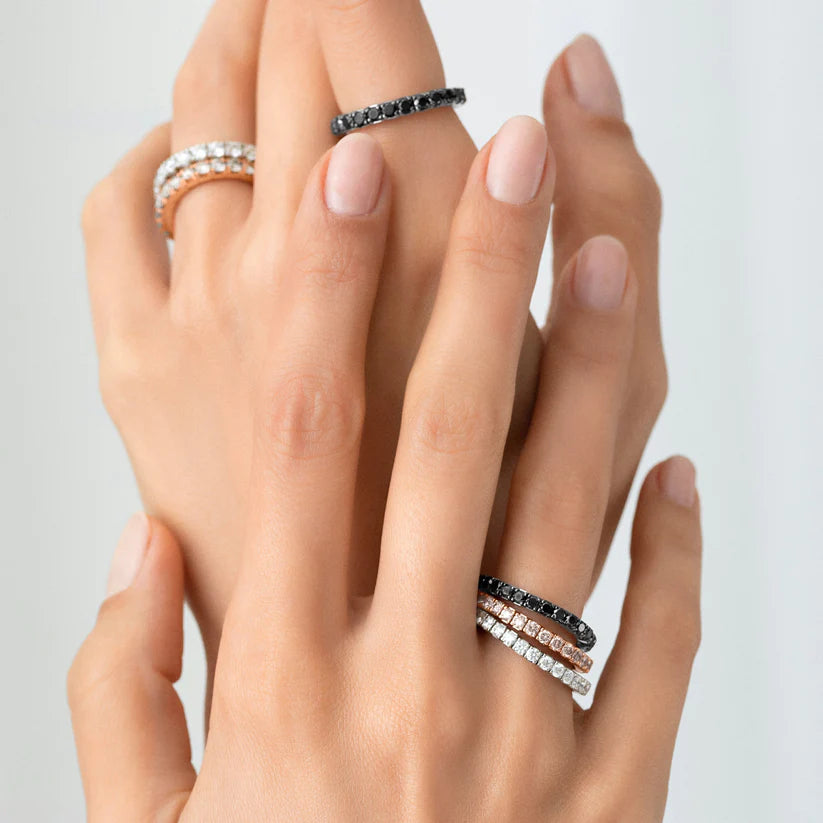 Multiple stretch diamond rings in black, white, and rose gold, on two inter-clasped hands